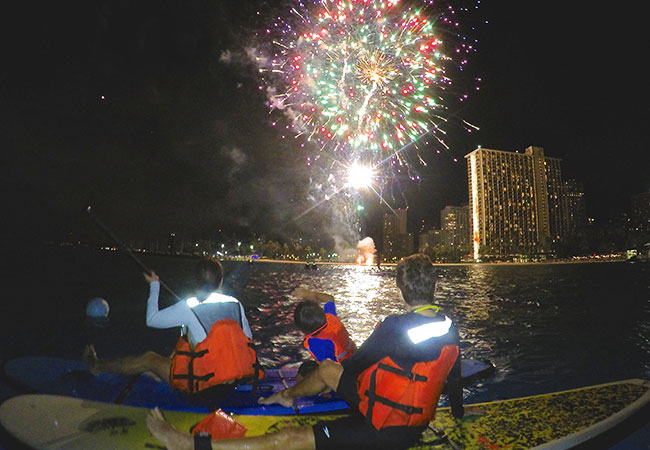 Family sit of paddleboards and view fireworks at night in Honolulu