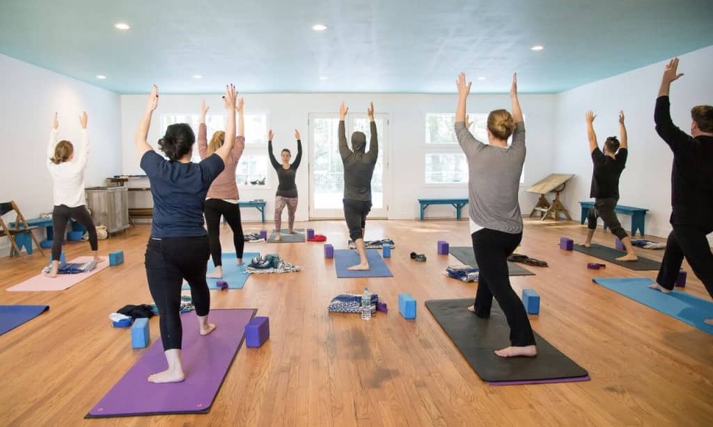 This is the Streamside Yoga Retreat in Andes, New York with a yoga class being led in a room with attendees doing a yoga pose.