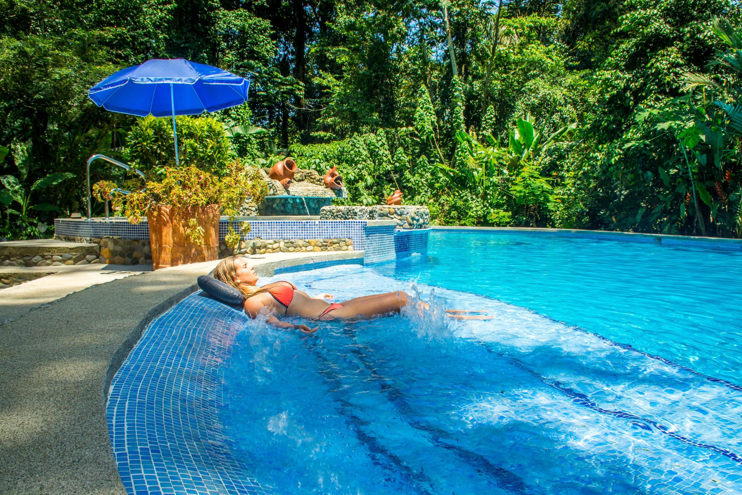 A woman relaxing in the pool surrounded by tropical rainforest beauty at The Goddess Garden in Costa Rica at their yoga retreat.