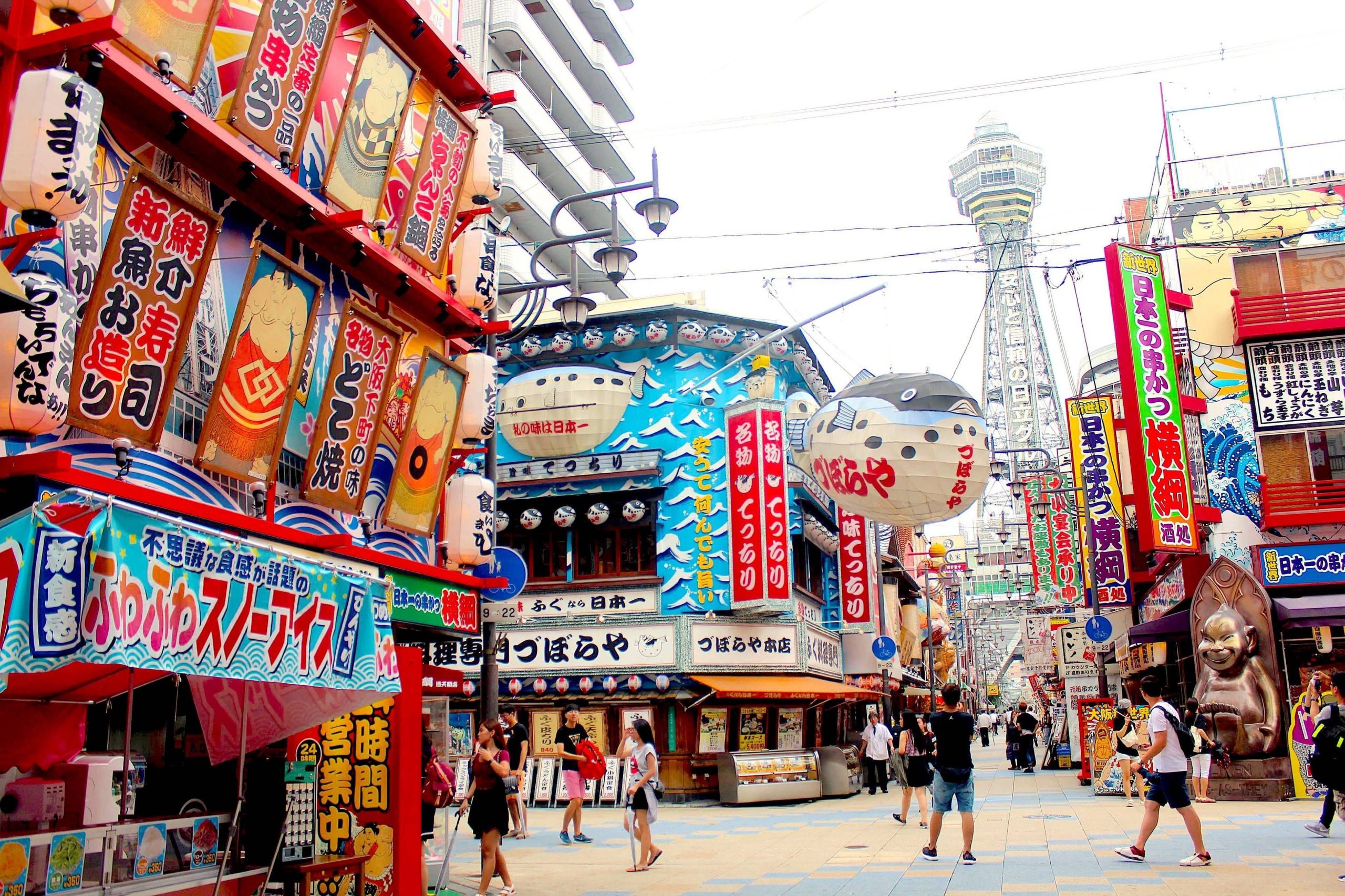 The brighly colored storefronts of the Shinsekai area of Osaka with a large pufferfish lantern in front of a restaurant