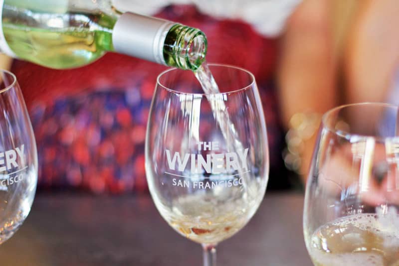 White wine being poured into a custom wine glass at The Winery SF tasting room where guests can taste some of the best wine in the region.