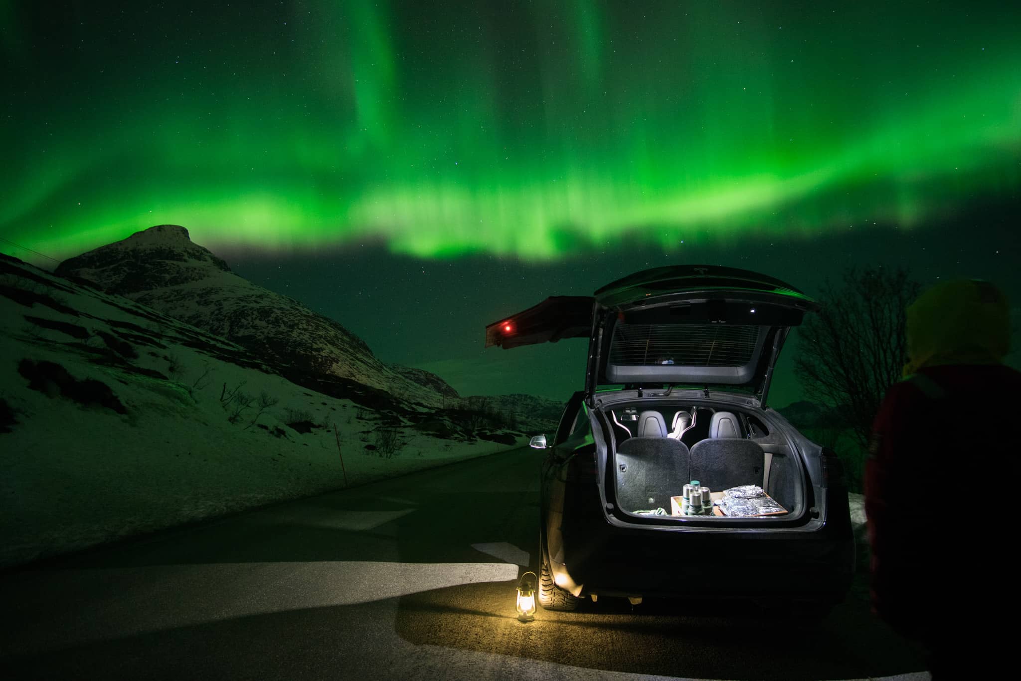 A Tesla model X opens as people watch the aurora.