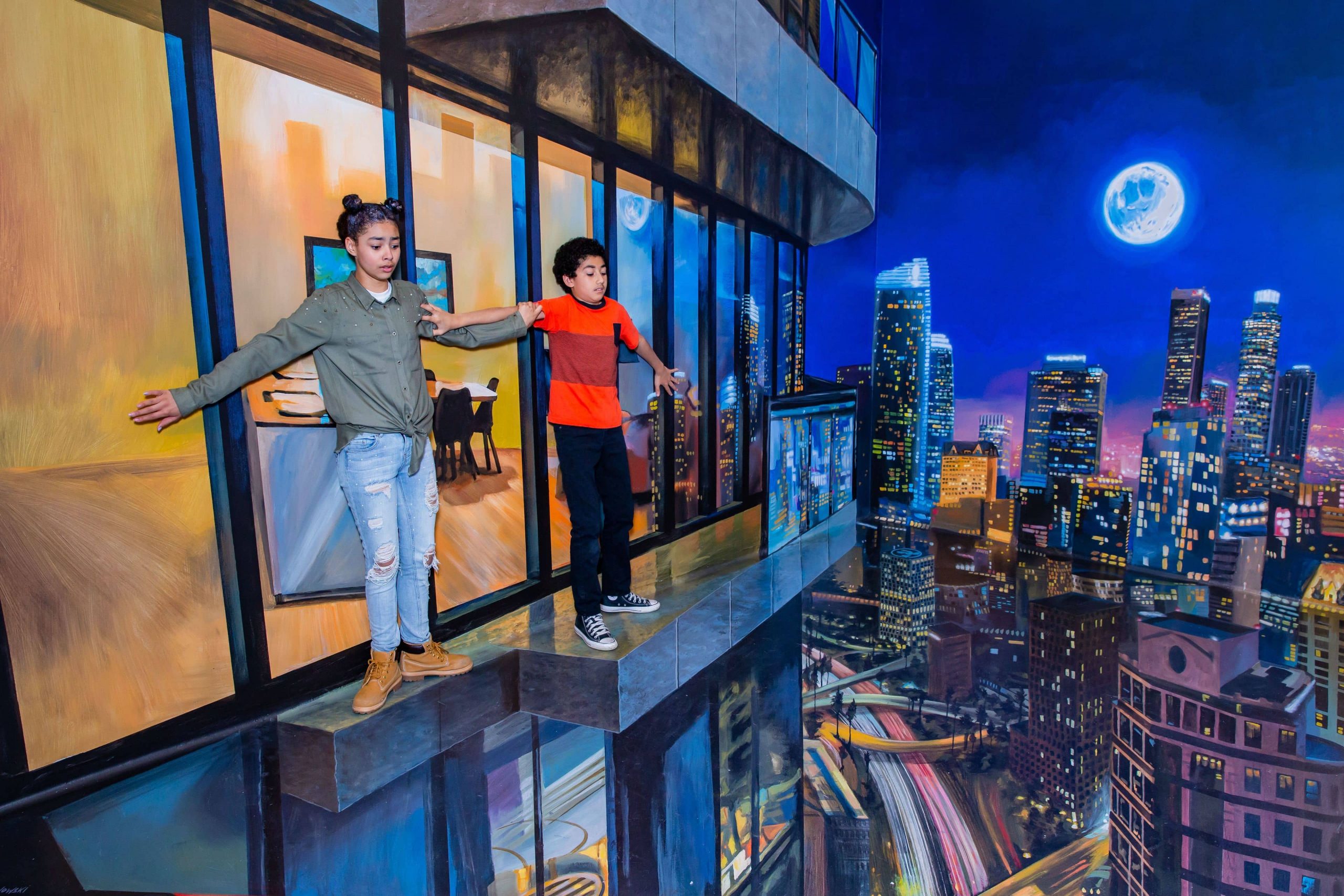 Two kids standing on the edge of a skyscraper in an optical illusion photo taken at the Museum of Illusions on a family vacation