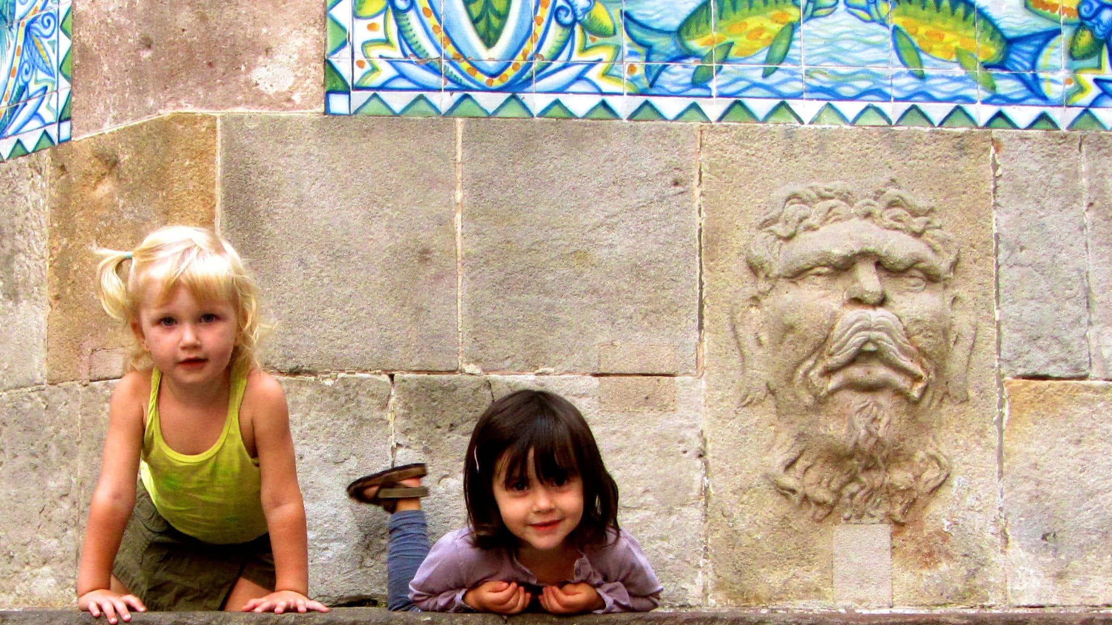 Two little girls posing with a funny face carved into the wall in Barcelona