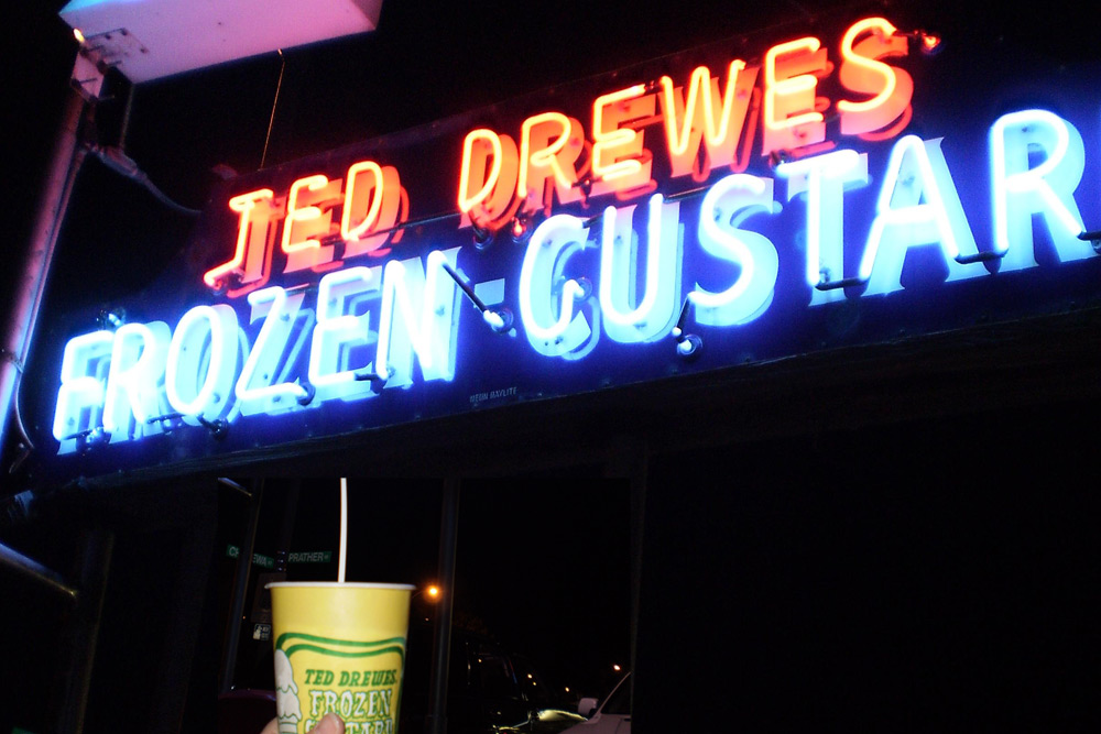 Yellow to-go cup with a spoon held under the neon sign at Jed Drewes Frozen Custard in St. Louis.