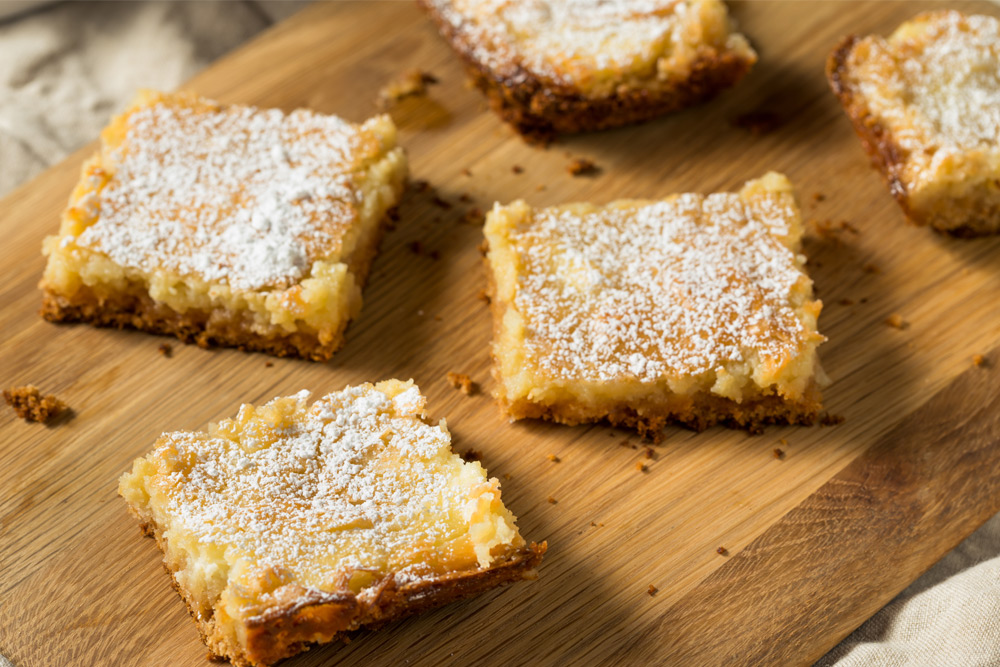 Homemade gooey butter cake with powdered sugar on a wooden cutting board—St. Louis's favorite dessert.