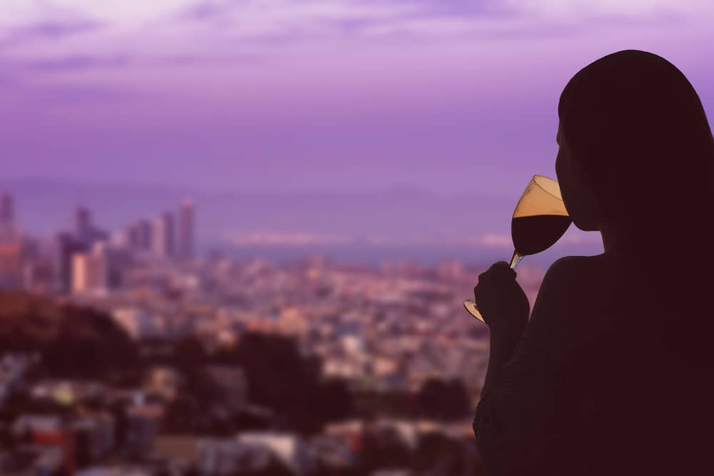 Female hand with glass of wine on San Francisco city background with a beautiful bright purple sunset occurs. 