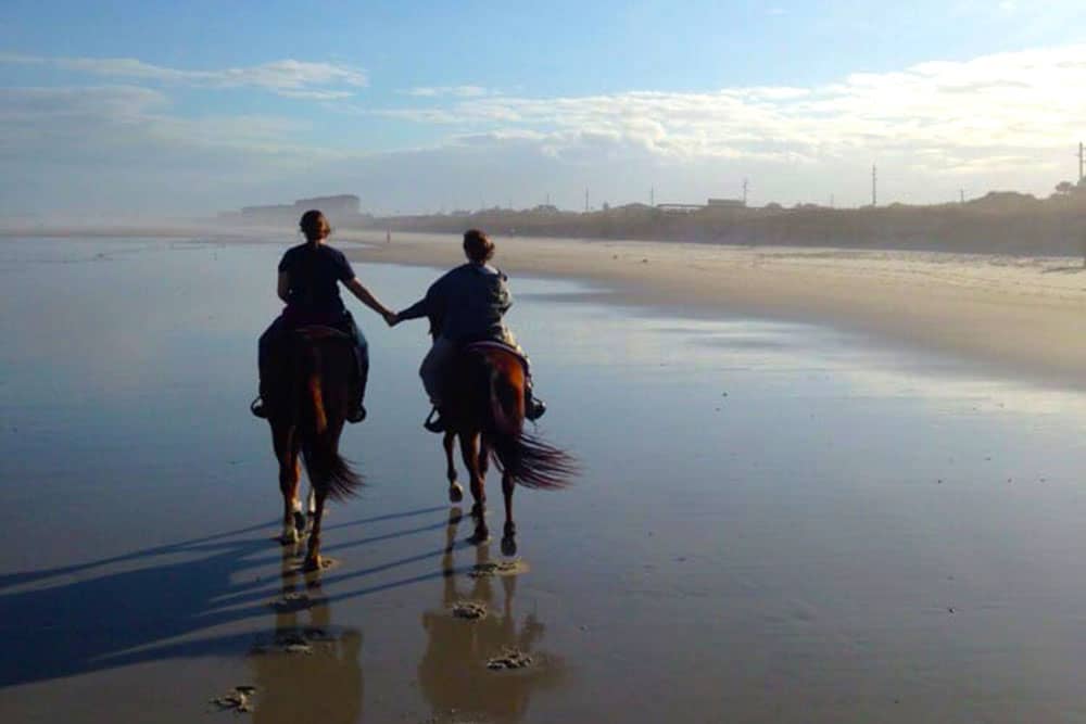 couple holding hands while horseback riding on fernandina beach on amelia island florida