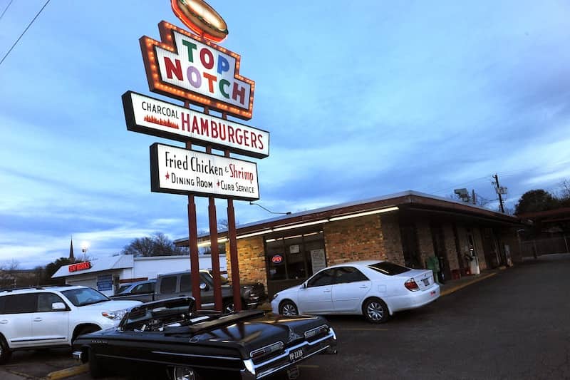 The view of Top Notch's colorful neon sign with cars in the parking lot below it.