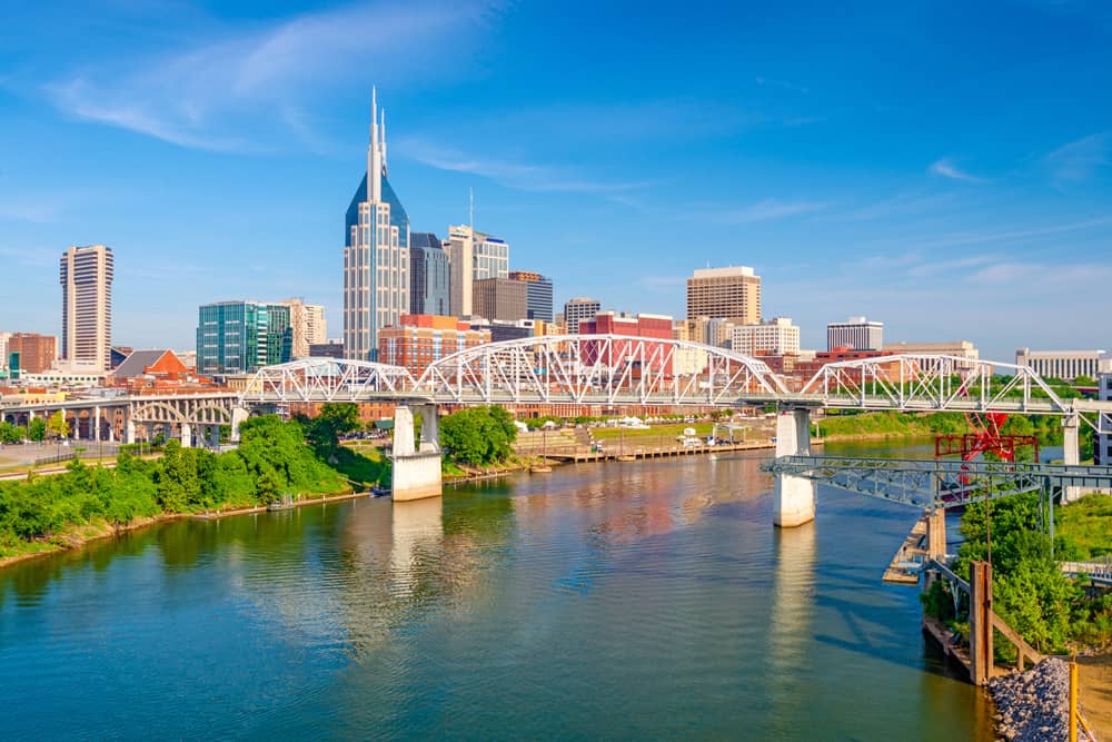 Skyline of downtown Nashville on a sunny day with a blue sky and Cumberland River in the foreground