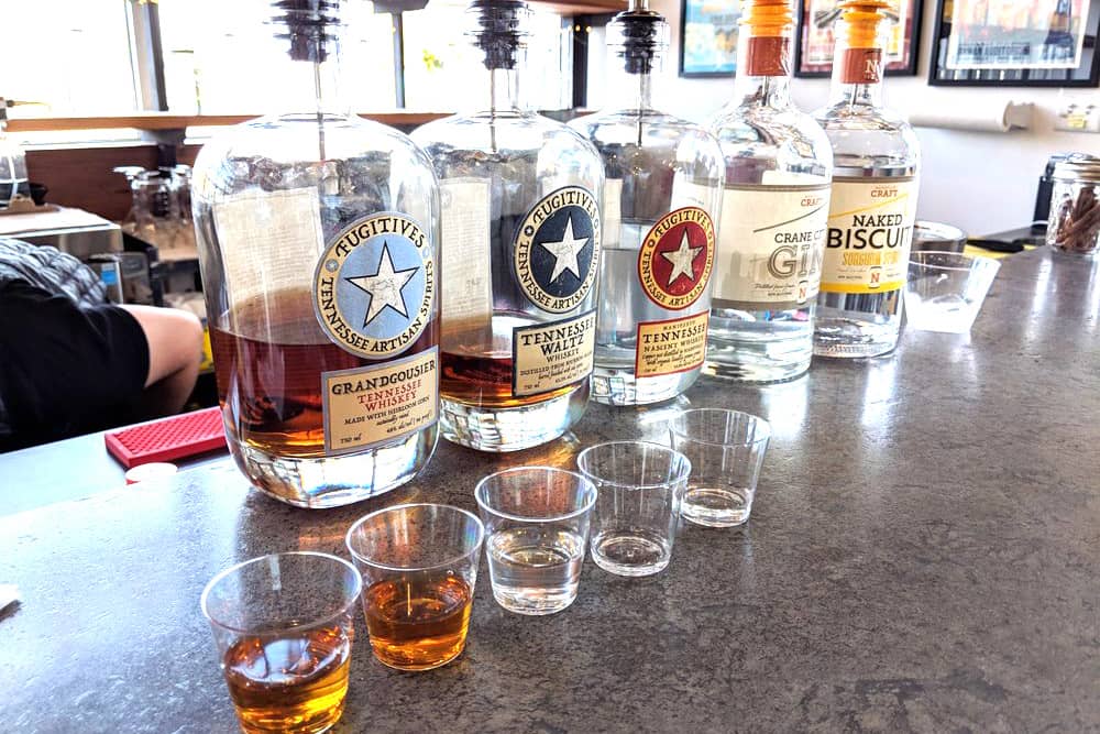 Five bottles of whiskeys and gin at Nashville Craft Distillery with tasting cups on the granite bar, ready for a Nashville bachelor party