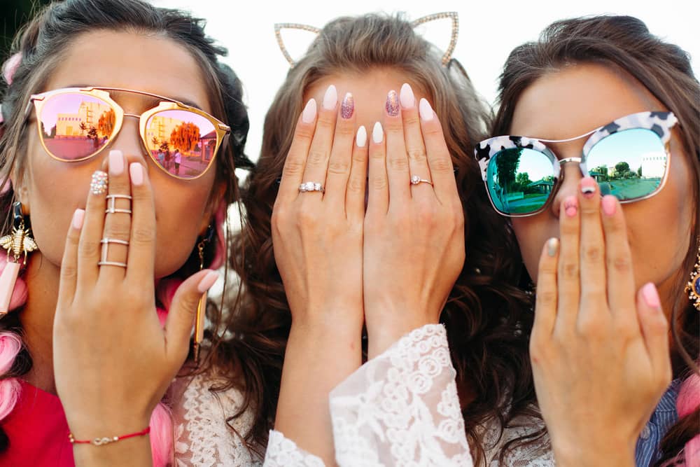 Three women wearing sunglasses show off their elaborate and colorful cameras for a bachelorette party in Las Vegas. 