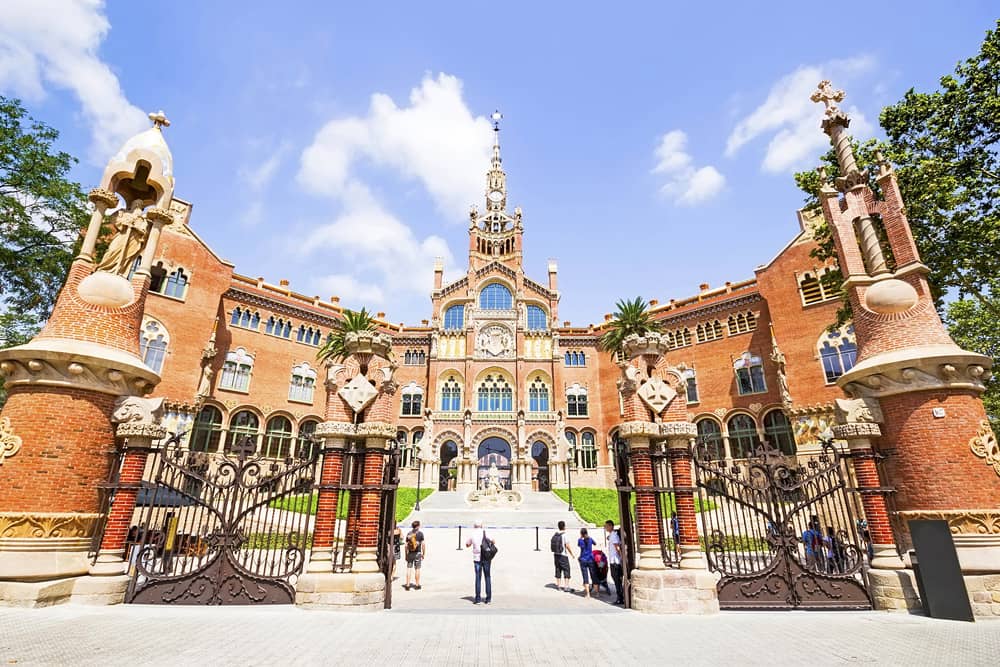 In front of the entrance to Hospital de la Santa Creu i Sant Pau, a red brick complex with sprawling gardens and an Art Nouveaux facade.