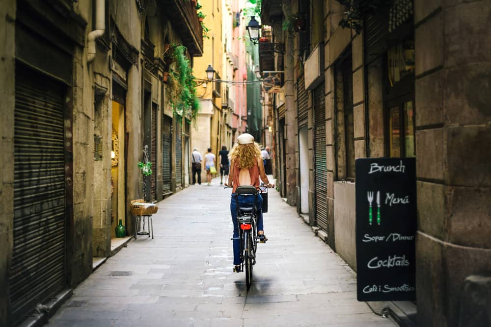 Getting around Barcelona is easy with a bike or public transportation Traveler riding a bike past a brunch cafe on a quiet street in Barcelona