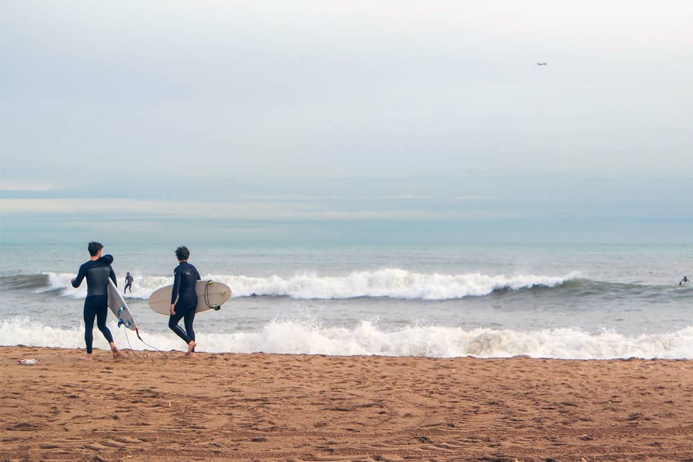 Three surfers in wetsuits heading into the waves at Barceloneta—a fun thing to do in Barcelona.