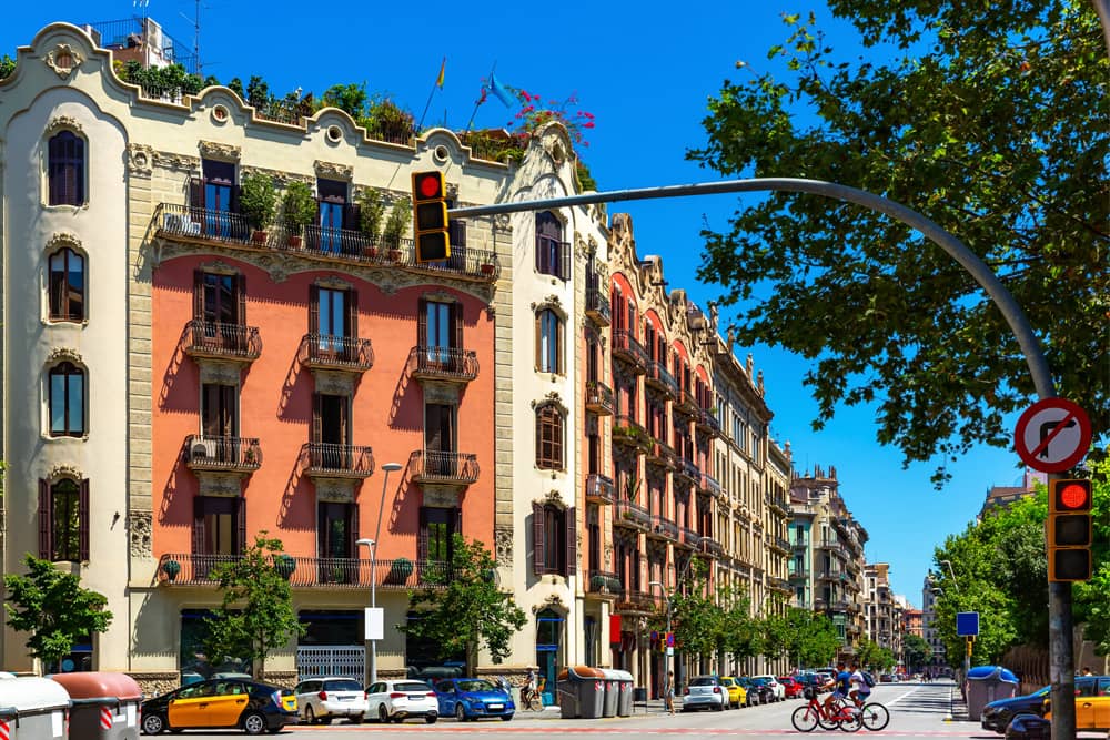 Colorful architecture in the chic Eixample district on a sunny day with lush green trees lining the streets.