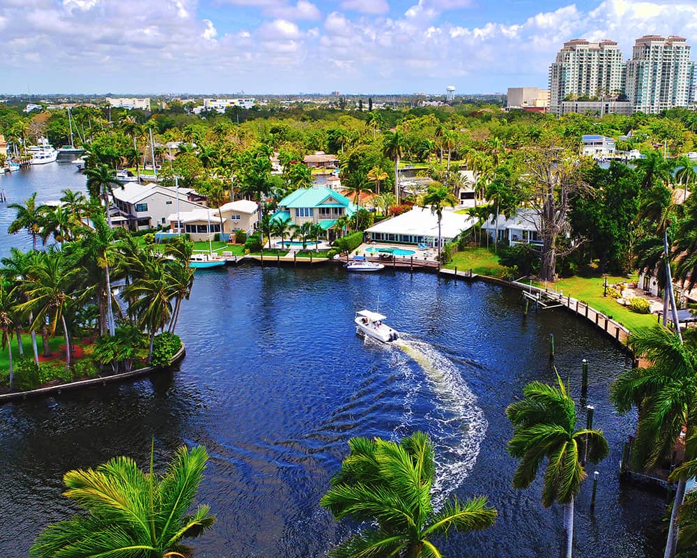 A boat cruises along a waterway surrounded by palm trees in Fort Lauderdale