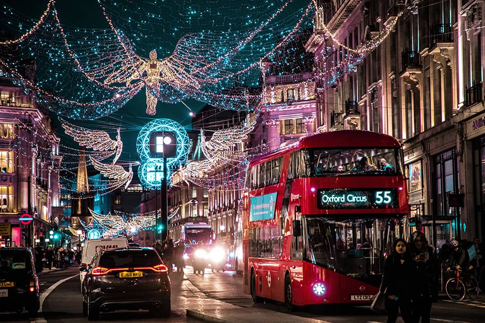 people stroll Regents Street at night in London as angels made from strings of lights stretch across the street