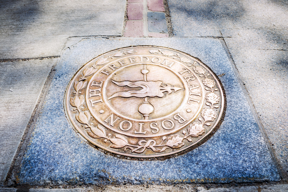 A metal emblem on the ground that says "The Boston Freedom Trail," a historic place Boston is known for.