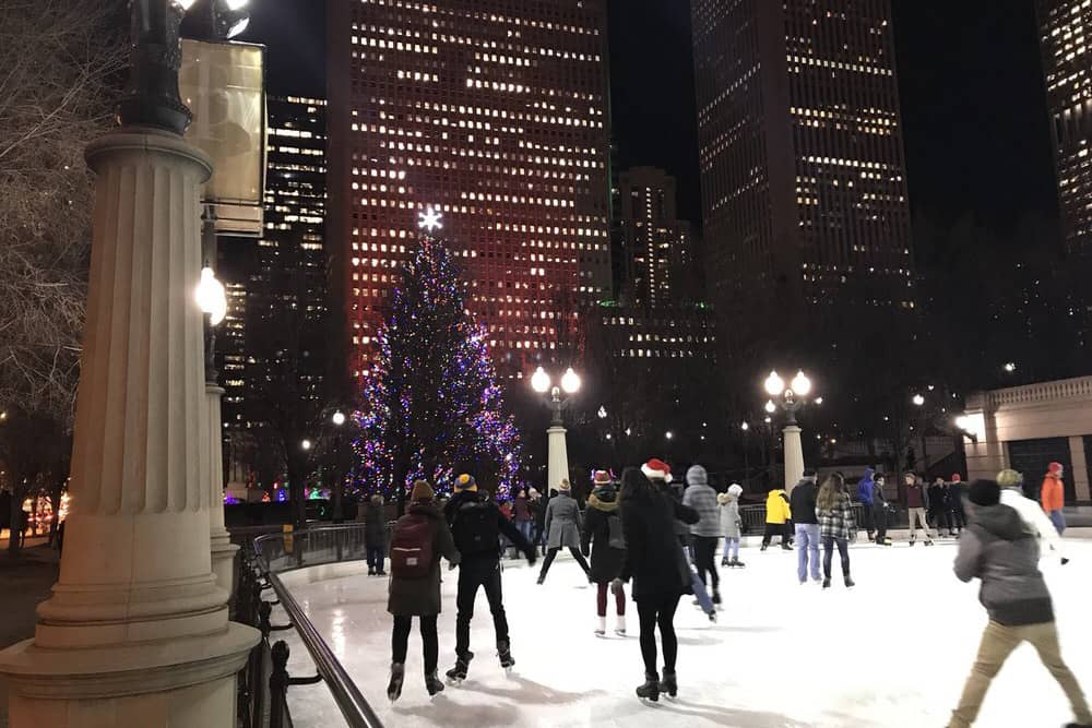 Groups of people ice skate around the rink in front of a Christmas tree in Chicago, where you’ll experience one of the best places to spend Christmas.
