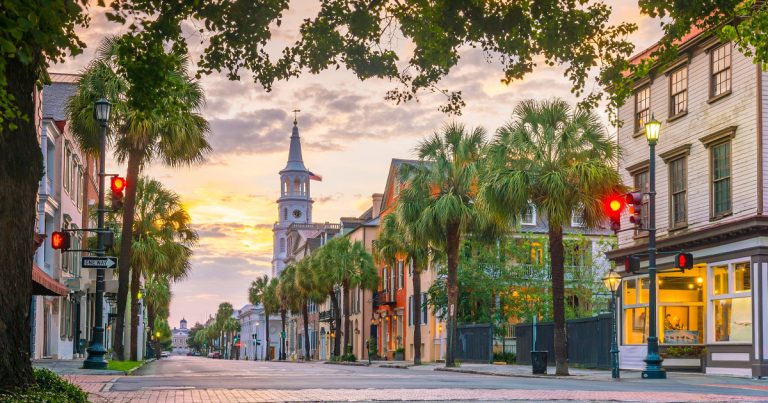 Romantic sunset light on a historical street in Charleston, lined with colorful buildings and palm trees.