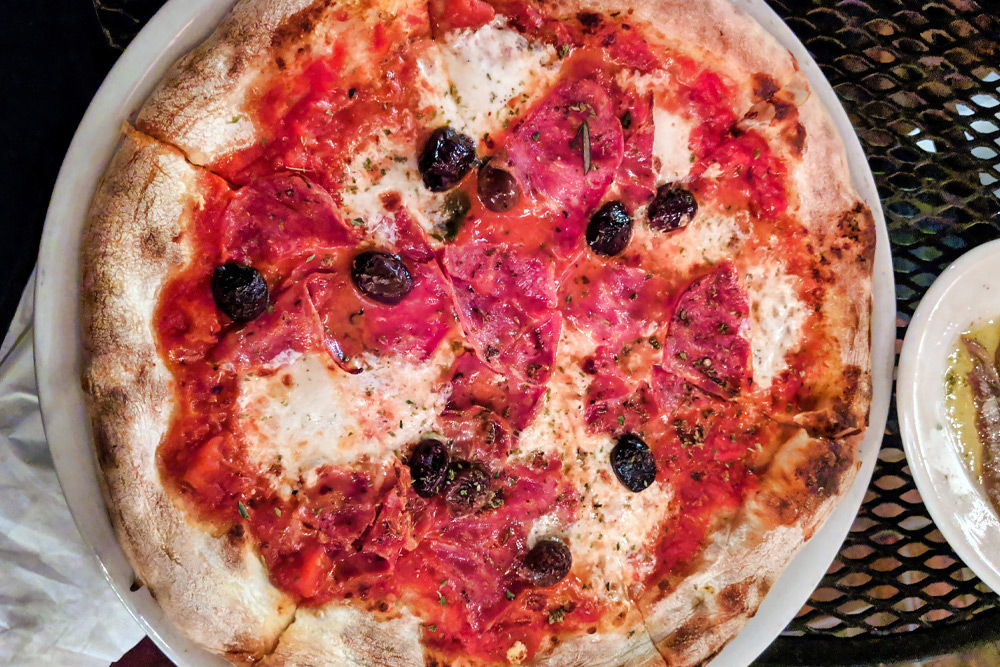 Pizza with olives, cheese, and prosciutto on a rustic crust from Pizzeria Bianco—one of the best date night restaurants in Phoenix
