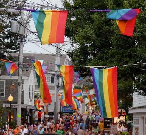 Rainbow Pride flags hanging over a busy street during Carnival in Provincetown