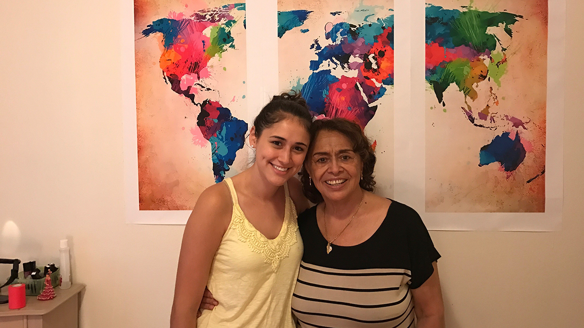 Veronica smiles next to her abuela (grandma) in front of a world map.