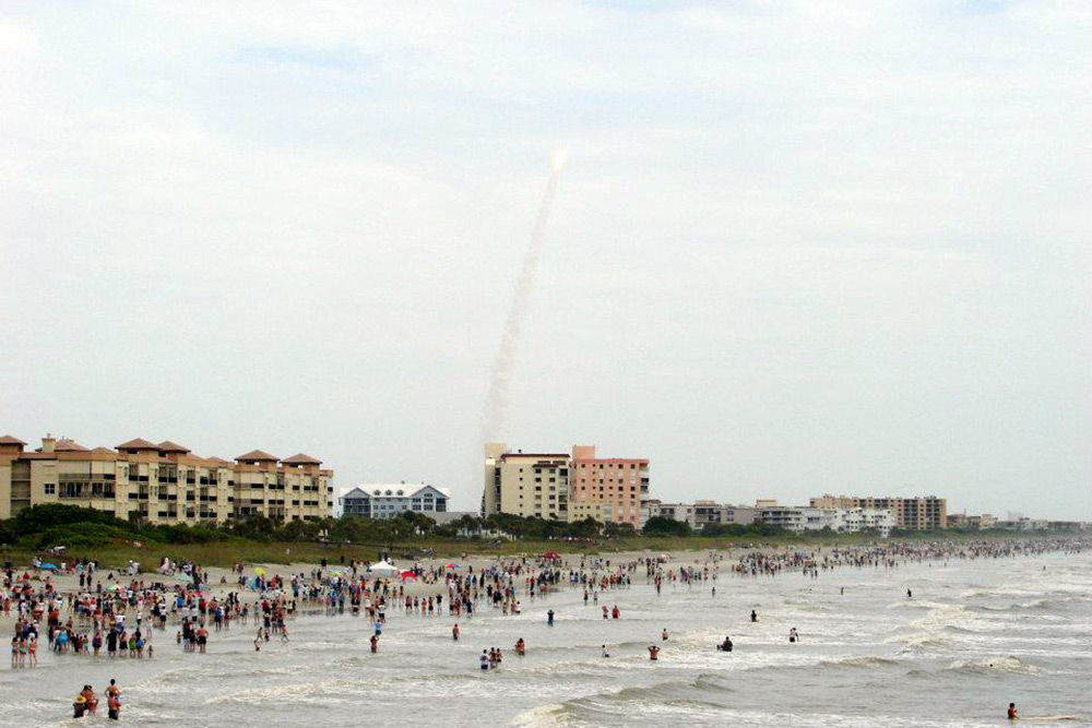 Space rocket shooting into the sky seen from the crowded shoreline at Cocoa Beach in Florida.