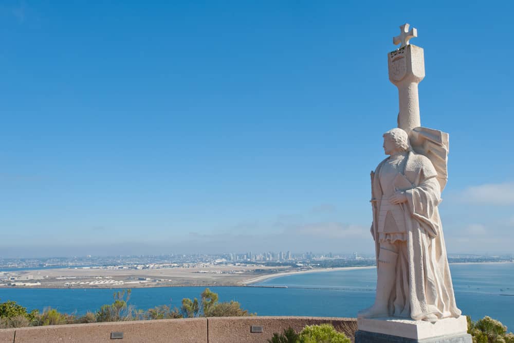 Statue of explorer Juan Rodríguez Cabrillo at Cabrillo National Monument with the backdrop of a blue sky, the Pacific Ocean, and the San Diego cityscape.