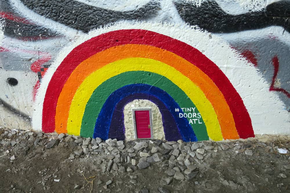 Tiny red door at the base of a wall surrounded by a rainbow painted over graffiti. Finding Atlanta's Tiny Doors is a fun free thing to do for families.