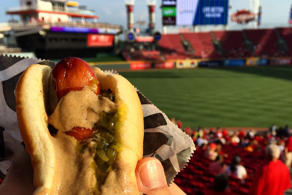 closeup of a hotdog with mustard and relish help up in front of the field at a baseball stadium during Spring Training in Arizona.