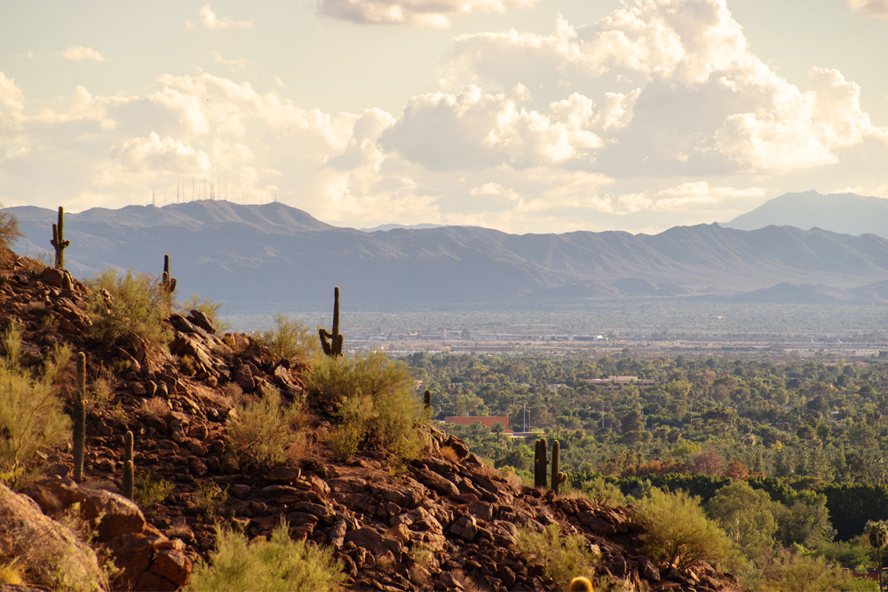 View of Phoenix and Tempe from Camelback Mountain on a day with scattered clouds and lush trees in the distance.