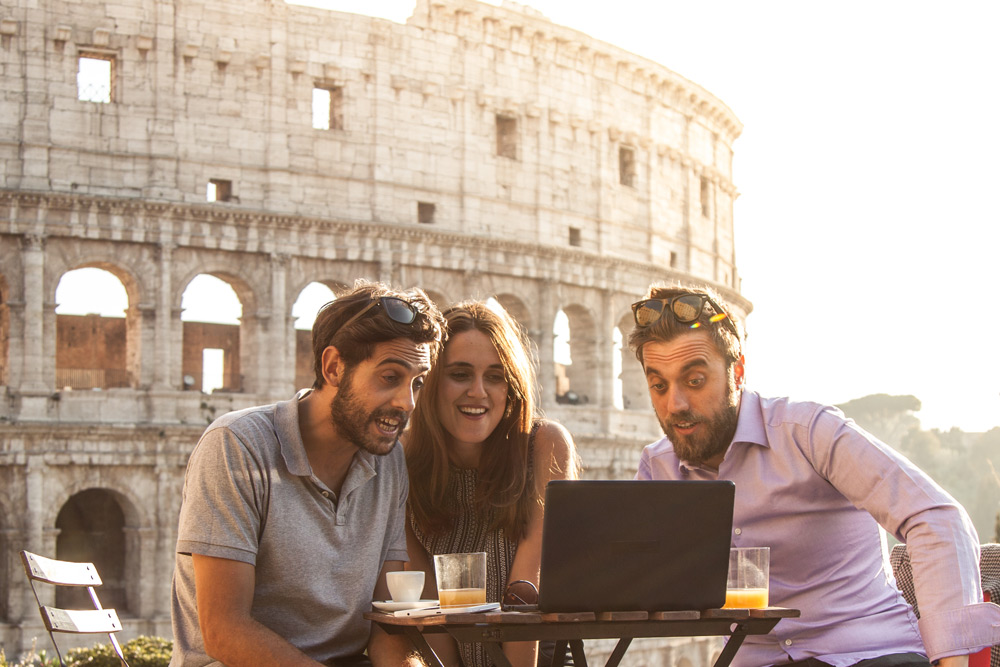 People learn Italian outside of the Coliseum. Learning the language is a top Rome travel tip. Three people practice speaking in Italian. Learning some phrases is a top travel tip.
