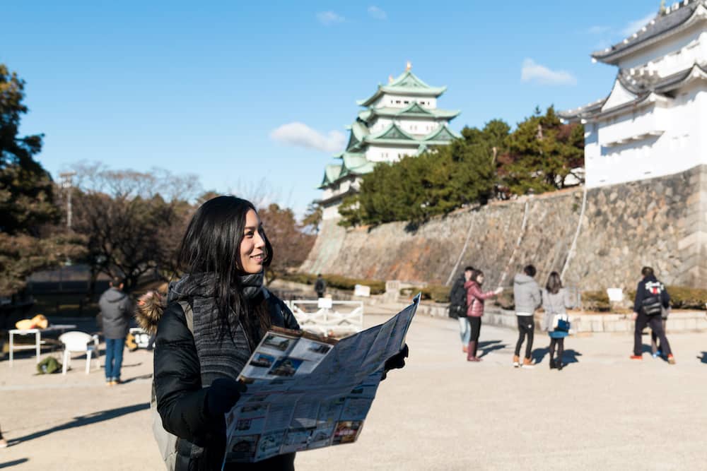 Solo travel to Japan is made easier when you learn and understand the cultures of different regions. Here, a woman reads a map while standing in front of Japan's Nagoya castle.