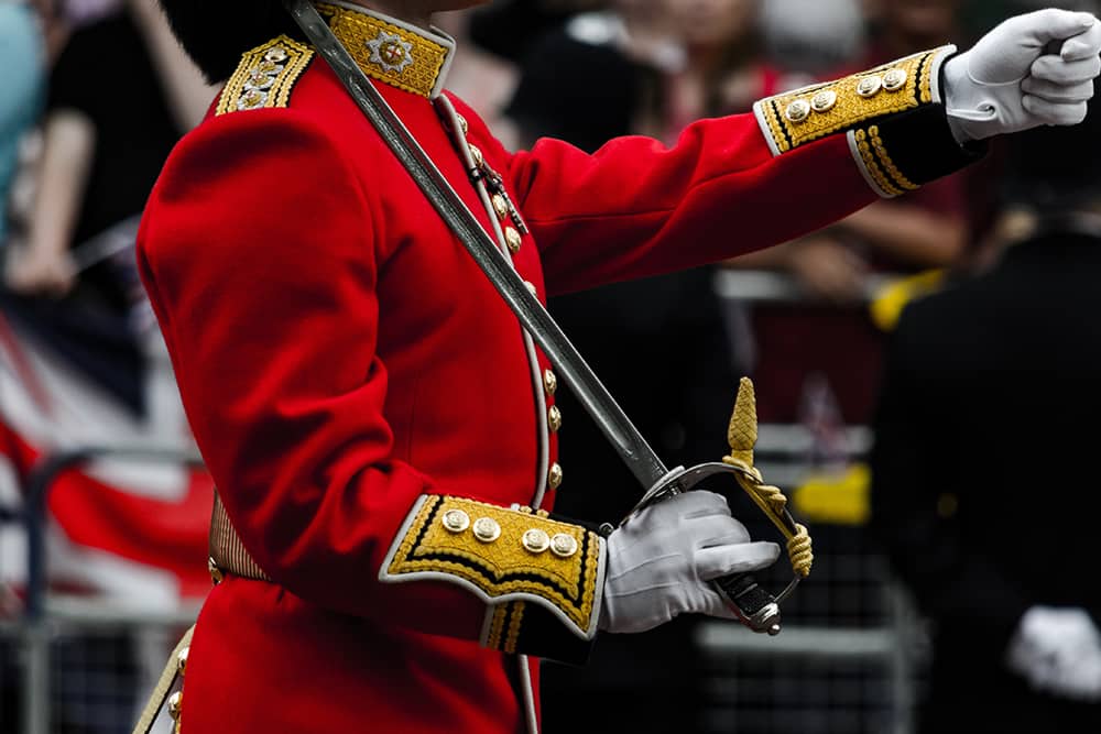 A London Guard in his traditional red uniform and saber resting on his shoulder is photographed mid-march