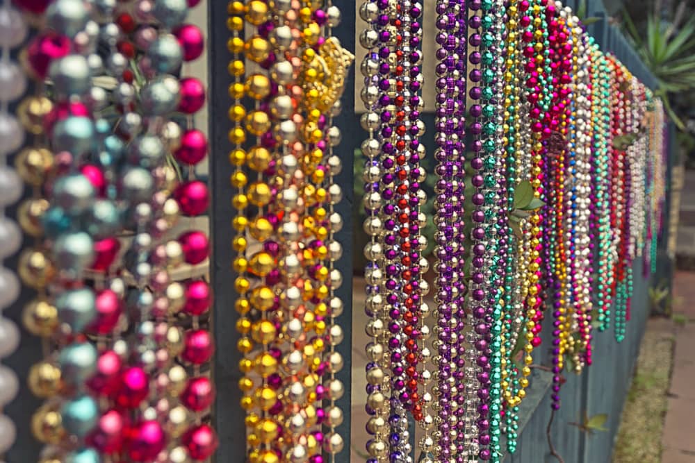 Several strands of colorful shiny beads hang from a fence in New Orleans—something you need to learn about for Mardi Gras