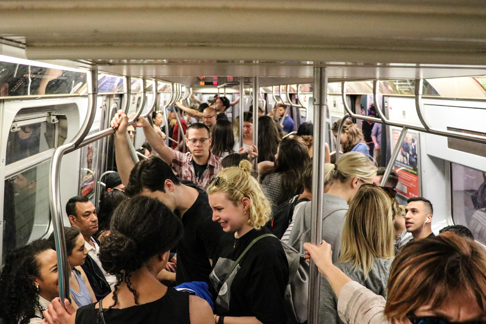  A group of NYCC fans on a well-lit subway train in New York City.