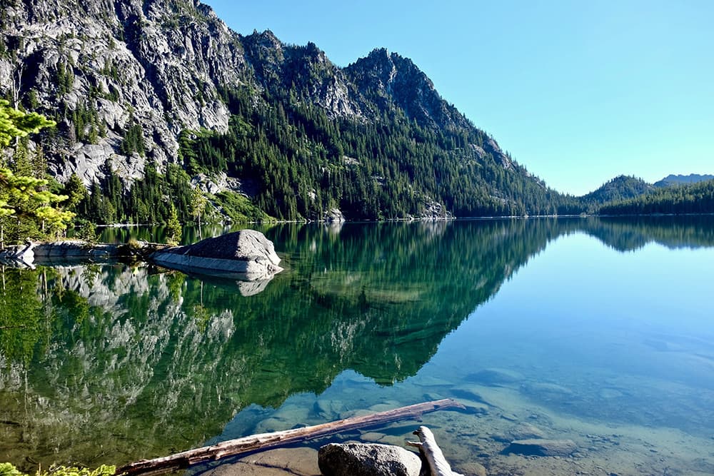 Glassy lake surface bordered by tree-covered rocky hills