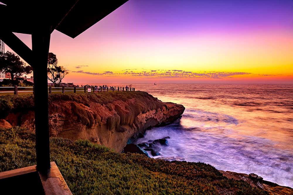 Pink, gold, and purple sunset over ocean and cliffs in San Diego