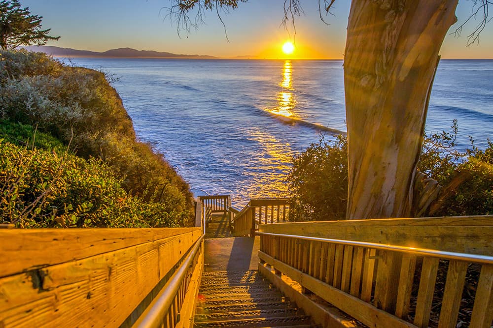Wooden stairs leading to the ocean as the sun sets in the distance in Southern California