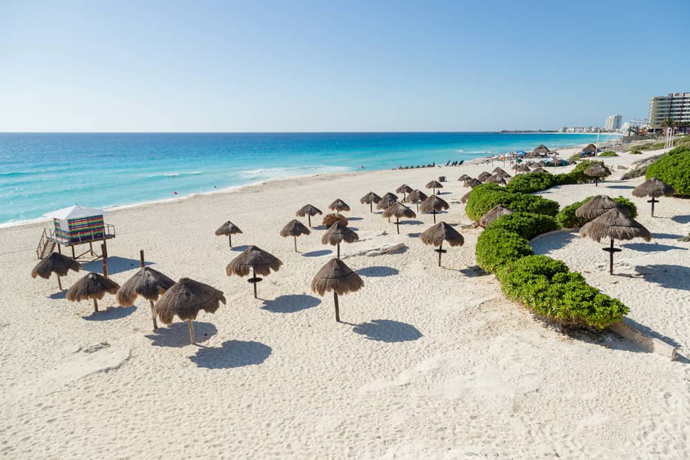 Grass-roofed cabanas dot the white sand at the beach during the dry season—the best time to visit Cancun