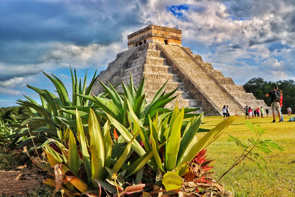 Travelers exploring pre-Columbian structure Chichen Itza with succulents in the foreground