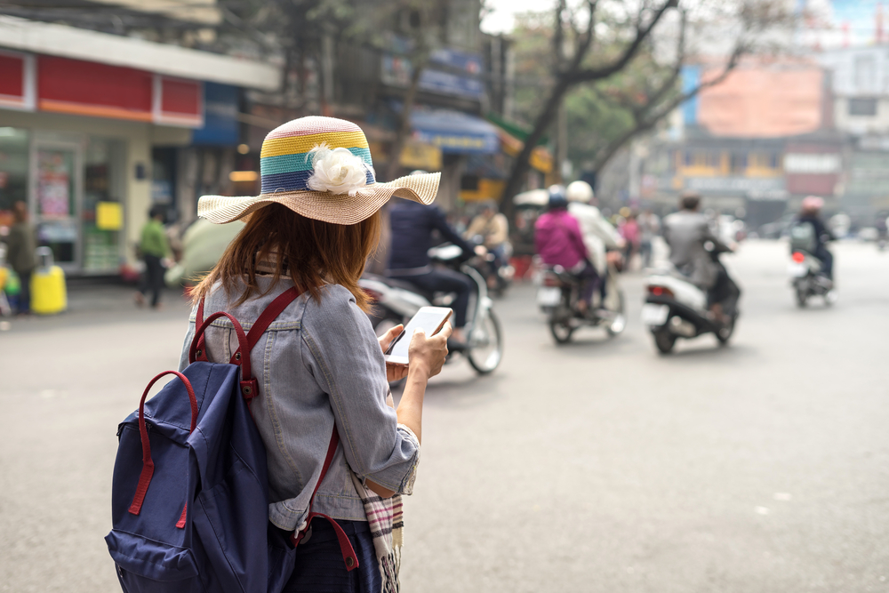 woman in hat using travel app on city street