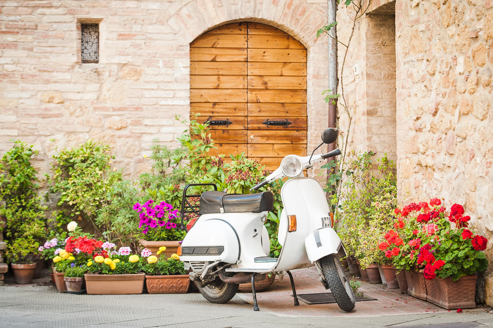A Vespa parked in front of potted flowers on a street in Rome. Riding a Vespa is a top travel tip for Rome.