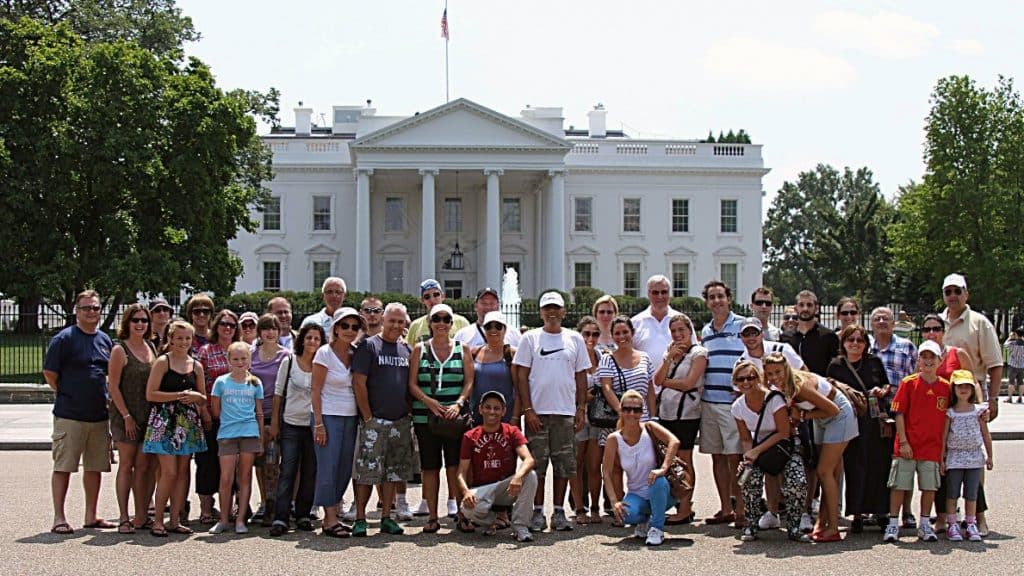 A group of people posing for a photo in front of a white house
Description automatically generated