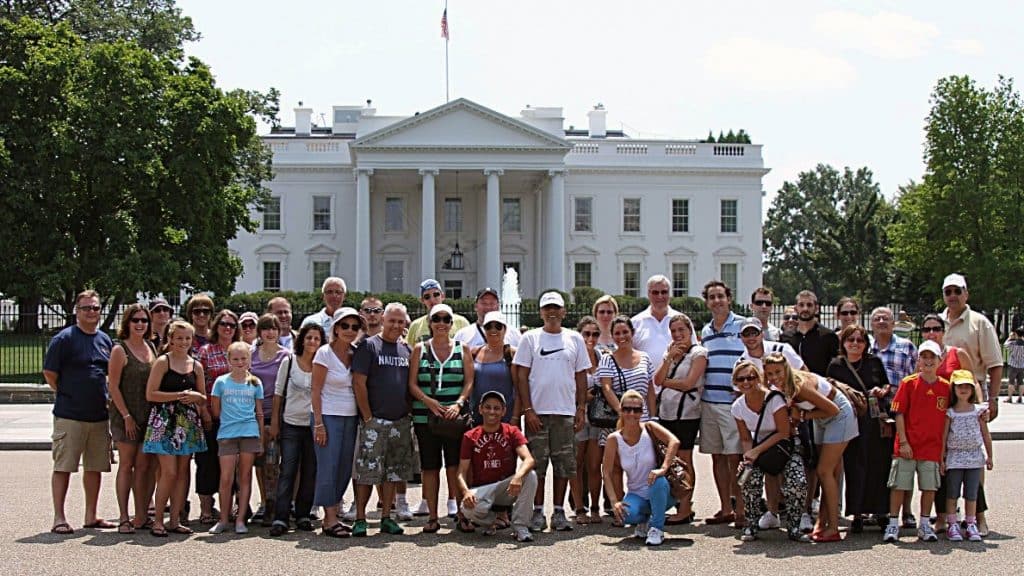 A group of people posing for a photo in front of a white house

Description automatically generated